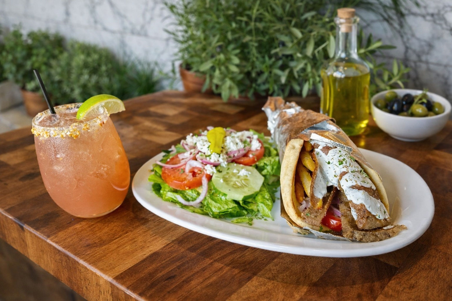 A gyro wrap with Greek salad and a craft cocktail on a wooden table at Yamas
